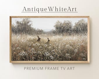 Puede incluir: Impresión artística enmarcada que presenta dos liebres en un campo de hierba alta y flores silvestres. La obra de arte tiene una paleta de colores neutros y un marco de madera marrón claro. Se muestra el texto "Antique White Art" y "Premium Frame TV Art".