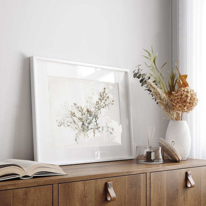 K&ouml;nnte beinhalten: Ein wei&szlig; gerahmter Druck einer botanischen Illustration eines Trockenblumenarrangements auf einem Holzregal mit einer Vase mit Trockenblumen und einer Diffuserflasche.