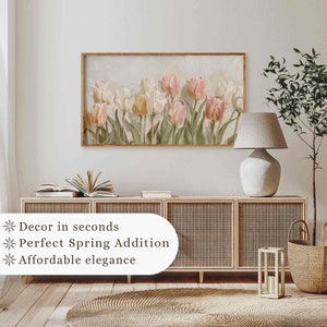 May include: A framed print of a watercolor painting of pink and white tulips with green leaves on a light background. The print is hanging on a white wall above a wooden cabinet with wicker doors.