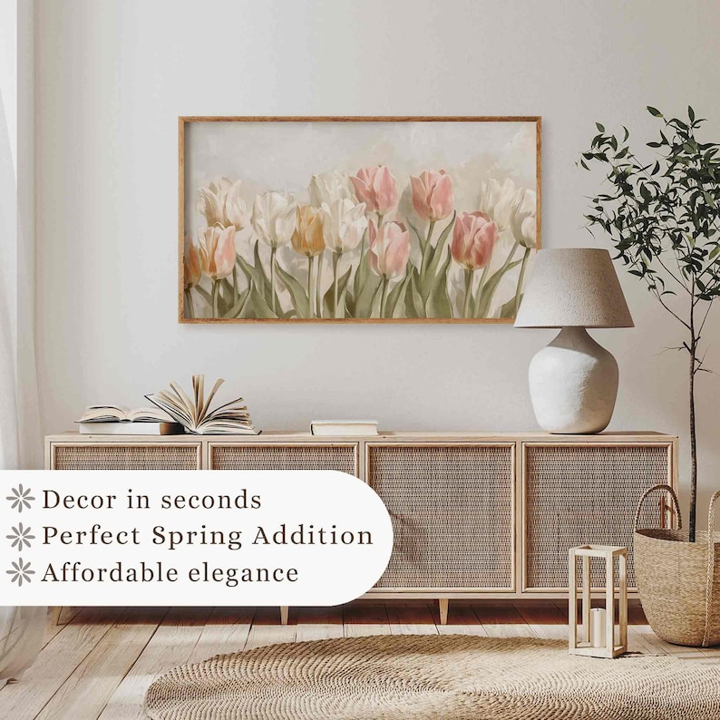 May include: A framed print of a watercolor painting of pink and white tulips with green leaves on a light background. The print is hanging on a white wall above a wooden cabinet with wicker doors.