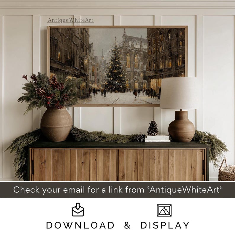 May include: A framed print of a European city street scene with a Christmas tree. The artwork is displayed above a wooden cabinet with a lamp, vase, and greenery. The text "AntiqueWhiteArt" is visible on the frame. The bottom of the image has the text "DOWNLOAD & DISPLAY".
