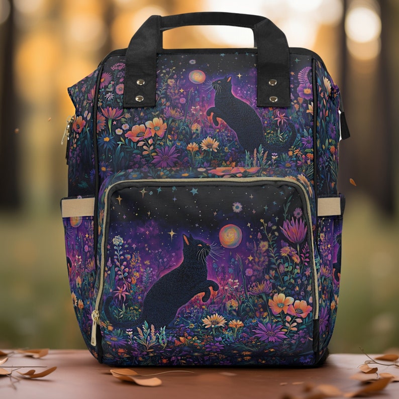 May include: Black backpack with a floral and starry design featuring two black cats. The backpack has a large main compartment and a smaller front pocket.