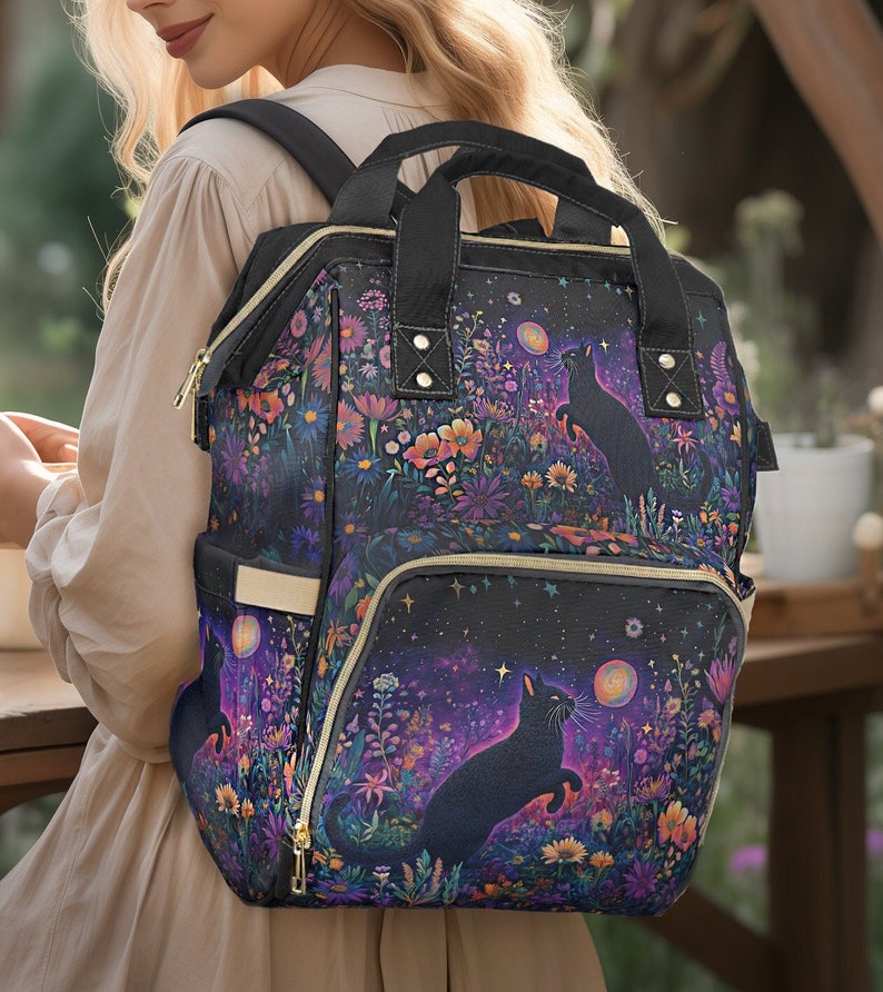 May include: A black backpack with a floral and starry design featuring two black cats. The backpack has multiple pockets and gold zippers.