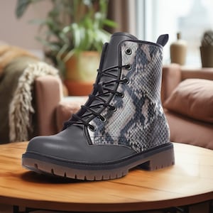 Könnte beinhalten: Schwarze Lederstiefel mit Schlangenmuster. Die Stiefel haben einen Schnürverschluss und eine dicke Sohle.