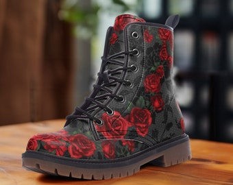 May include: Black combat boot featuring a red rose pattern on a gray background. The boot has black laces, a round toe, and a brown sole. The floral design covers the entire boot, creating a striking visual.