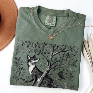 Peut inclure: Un t-shirt vert avec une illustration en noir et blanc d'un renard dans un arbre. Le t-shirt porte le texte "COMFORT COLORS" et "S - P - CH" sur l'&eacute;tiquette.