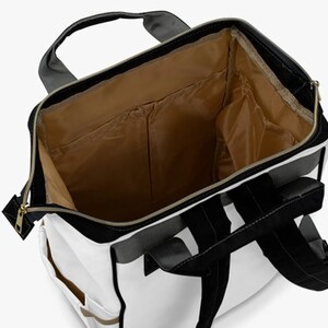 May include: A white backpack with black and gray accents. The backpack has a large main compartment and several smaller pockets. The interior of the backpack is lined with a brown fabric.