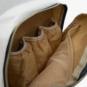 May include: The inside of a white backpack with multiple pockets. The pockets are made of a beige fabric with a mesh lining. The backpack has a zipper closure.