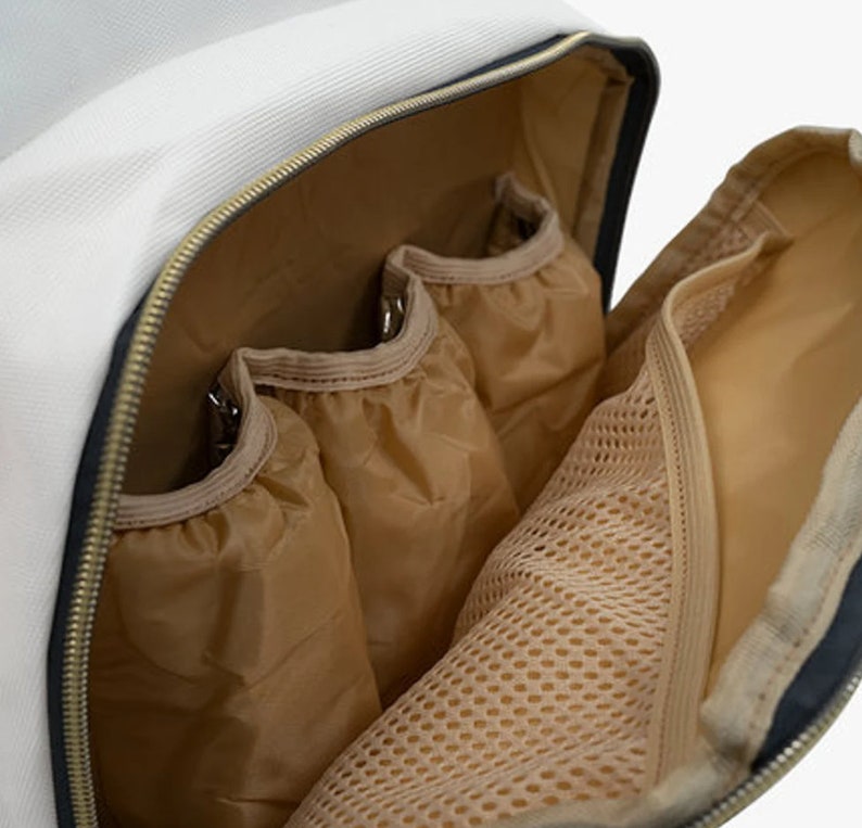 May include: The inside of a white backpack with multiple pockets. The pockets are made of a beige fabric with a mesh lining. The backpack has a zipper closure.