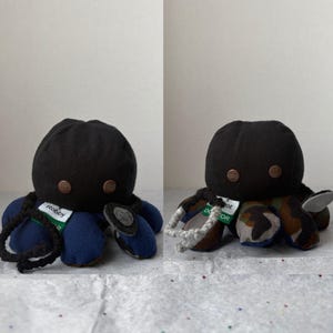 May include: Two plush octopus toys with black heads and copper-coloured eyes. One has blue and black tentacles, the other has camouflage and grey tentacles. Each has a tag with text.