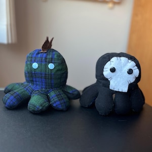 Puede incluir: Dos juguetes de peluche de pulpo. Uno es negro con una cara de calavera blanca y el otro es de cuadros verdes y azules con un mechón marrón en la parte superior.