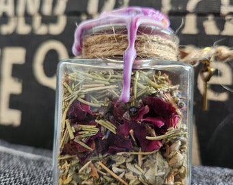 Könnte beinhalten: Ein kleines Glasgefäß mit einem violetten Wachssiegel und einer Schnur, die um den Deckel gebunden ist. Das Gefäß ist gefüllt mit getrockneten Kräutern und Blumen, darunter Lavendel, Rosmarin und Rosenblätter.