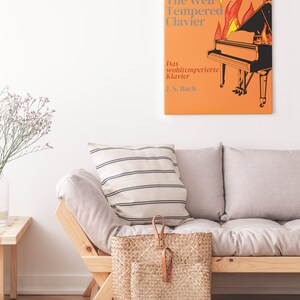 May include: A white couch with a striped pillow and a wicker basket. A framed print of a piano on fire with the text "The Well-Tempered Clavier" and "Das wohltemperierte Klavier J.S. Bach" is hanging on the wall.
