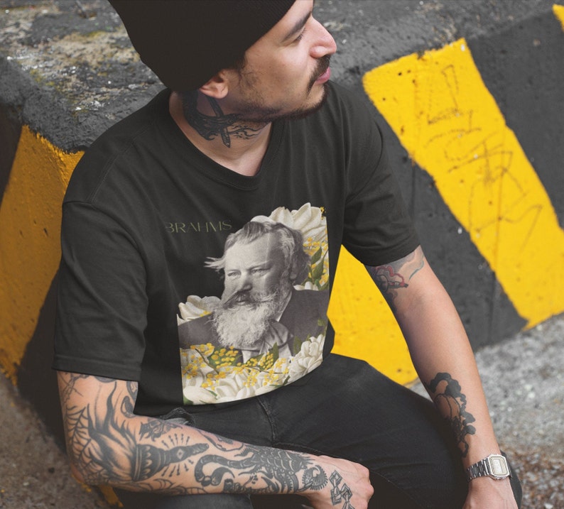 May include: A black t-shirt with a graphic of Johannes Brahms surrounded by white flowers and the text "Brahms" printed on the front.