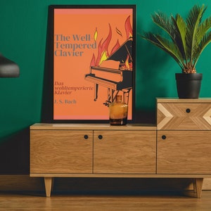 May include: A vintage-style poster with an orange background featuring a black and white illustration of a grand piano with flames behind it. The text on the poster reads "The Well Tempered Clavier" and "Das wohltemperierte Klavier J.S. Bach". The poster is displayed on a wooden shelf with a green wall behind it.