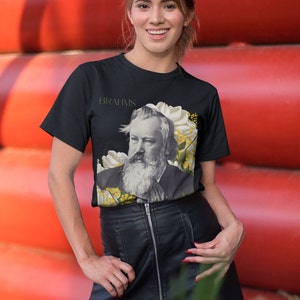 May include: A black t-shirt with a graphic of Johannes Brahms, a German composer, surrounded by white and yellow flowers. The text "BRAHMS" is printed above the image.