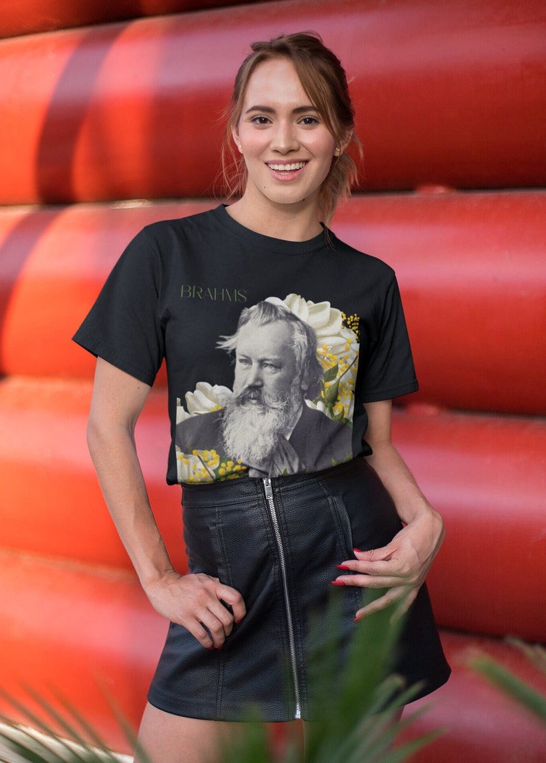 May include: A black t-shirt with a graphic of Johannes Brahms, a German composer, surrounded by white and yellow flowers. The text "BRAHMS" is printed above the image.