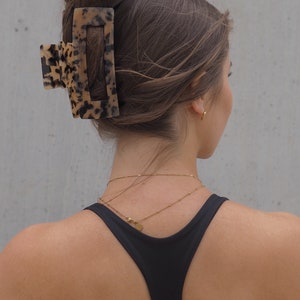 May include: A woman with brown hair wearing a black tank top and a gold chain necklace. Her hair is pulled back with a large tortoiseshell hair claw.