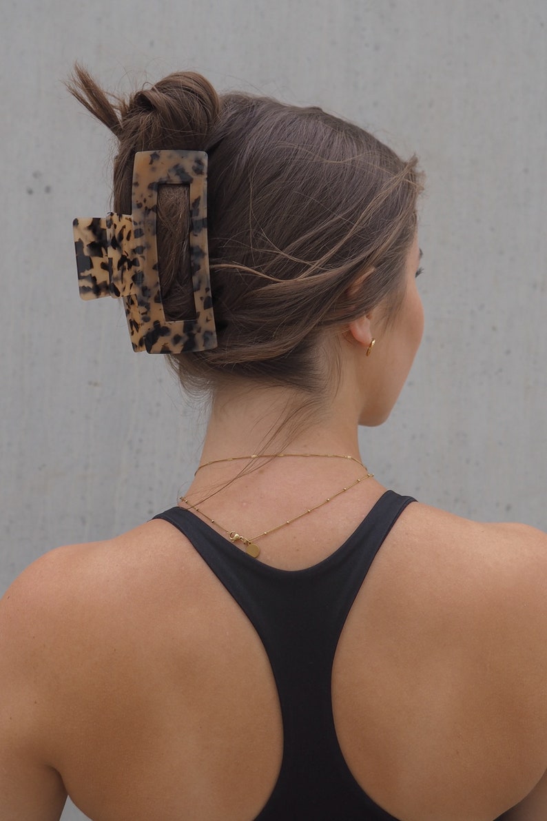 May include: A woman with brown hair wearing a black tank top and a gold chain necklace. Her hair is pulled back with a large tortoiseshell hair claw.