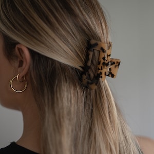 May include: A tortoiseshell hair clip with a rectangular shape. The clip is in a woman's hair.