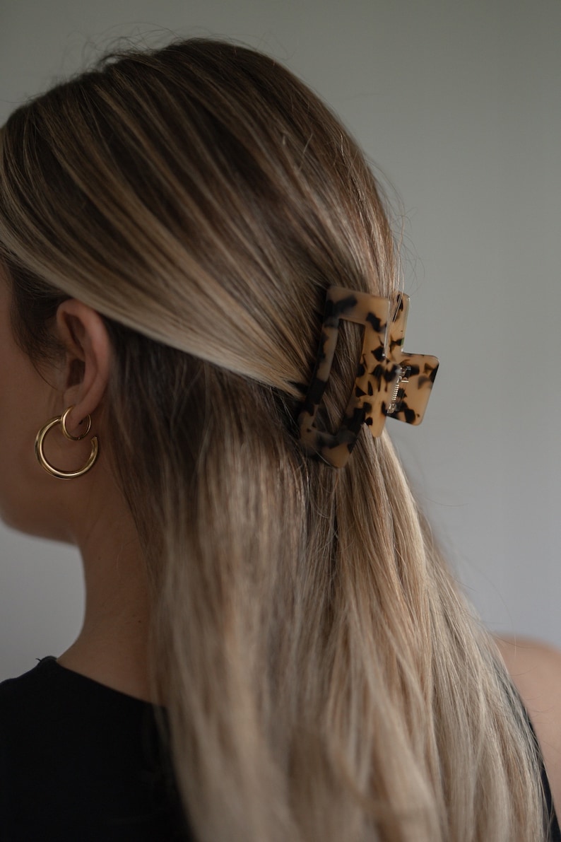 May include: A tortoiseshell hair clip with a rectangular shape. The clip is in a woman's hair.