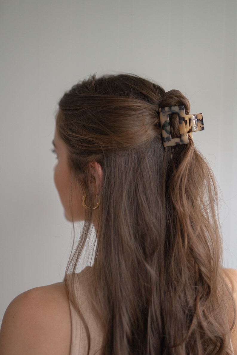 May include: A tortoiseshell hair clip with a square shape, holding back a woman's long brown hair.