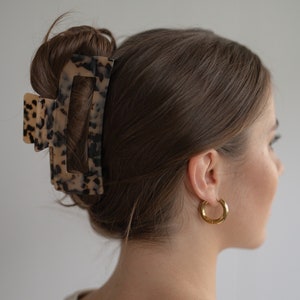Può includere: Un fermaglio per capelli rettangolare di tartaruga marrone e nero. Il fermaglio tiene i capelli marroni di una donna in uno chignon.