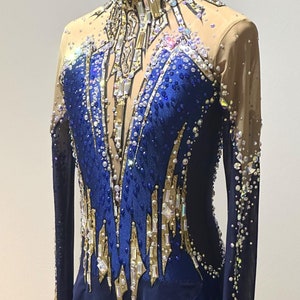 May include: A navy blue and gold leotard with long sleeves, designed for rhythmic gymnastics. The garment features intricate crystal and sequin embellishments, with a sheer nude mesh upper bodice and sleeves. The design includes a high neckline and a skirted bottom.