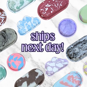 Peut inclure: Assortiment de plateaux et de sous-verres en résine de différentes formes, ovales, en forme de nuage et rondes, avec des motifs marbrés et colorés. Le texte "ships next day!" est écrit en lettres violettes sur un fond blanc.