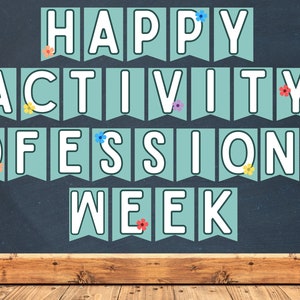 Puede incluir: Una pancarta azul verdosa con letras blancas que deletrean "Happy Activity Professionals Week" con flores coloridas decorando la pancarta.