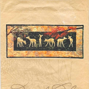 May include: A quilt pattern titled "Beneath the Boughs" featuring deer silhouettes under a tree with red and orange leaves. The dimensions are 74.3 cm x 32.4 cm. The packaging is tan with the words "Pine Needles" and the designer's name.