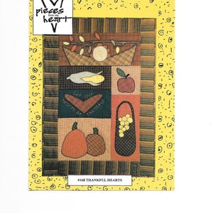 Puede incluir: Un edredón de retazos con un fondo amarillo y un diseño con elementos de la cosecha de otoño. El edredón incluye imágenes de una cornucopia, una manzana, calabazas y el texto "Let our hearts be thankful." El texto "#168 THANKFUL HEARTS" también es visible.