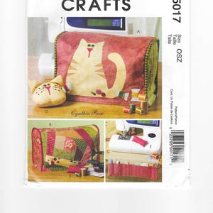 May include: McCall's Crafts sewing pattern featuring a cat design. The pattern includes instructions for a sewing machine cover and other accessories. The cover is primarily red with a cat applique and green trim. The pattern is designed by Cynthia Rose.