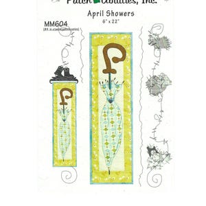 Könnte beinhalten: Stoffpaneel mit dem Text "April Showers" und den Maßen 15 cm x 56 cm. Das Paneel zeigt ein Schirmdesign mit braunem Griff und einem blau-grünen Musterdach. Das Paneel ist Teil einer zwölfteiligen Serie.