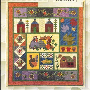 Puede incluir: Un edredón de retazos con temática otoñal, con el texto "FALL FESTIVAL" y "ART TO HEART". El edredón muestra varios cuadrados con imágenes de casas, hojas, calabazas y un pavo, todo en colores otoñales.