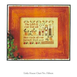 May include: Cross-stitch pattern titled "The Harvesters" by Little House Needleworks. The framed design features a family, pumpkins, and the Bible verse Deuteronomy 16:15. The frame is a warm, reddish-brown color.