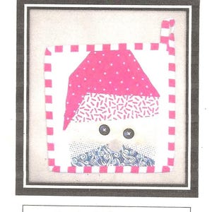 Puede incluir: Un agarrador de Santa con un gorro rosa y barba blanca. El agarrador está enmarcado y tiene un tamaño final de 20 cm x 20 cm. El gorro tiene lunares blancos y la cara tiene ojos de botón.