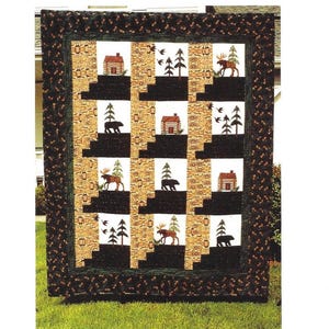 Puede incluir: Una colcha acolchada con temática de bosque. La colcha presenta un patrón repetido de cabañas, árboles y vida silvestre, incluyendo alces y osos. El borde es marrón oscuro con un estampado floral. El texto "Our Neck of the Woods Snuggler" está en la parte superior.