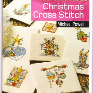 May include: A book cover titled "Twenty to Stitch Christmas Cross Stitch" by Michael Powell. The cover is pink with a gold border and features several small, square cross-stitch designs with Christmas themes, including ornaments, candles, and a decorated house.
