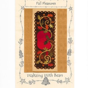May include: A rectangular fabric art piece with a central design of a red pumpkin surrounded by autumn leaves and vines. The words "Fall Pleasures" and "Waltzing With Bears" are written on the piece. The background is tan.