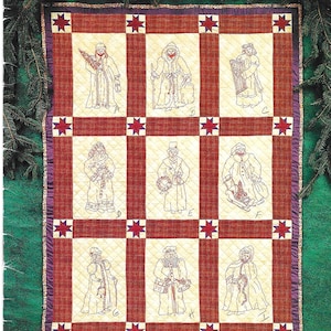 Pode incluir: Um padrão de colcha intitulado Old World Santas in Redwork por Marge Wooters da Indygo Junction, Inc. A colcha apresenta uma grade de nove quadrados cor de creme, cada um com uma figura de Papai Noel bordada em vermelho rotulada de A a I, separada por faixas xadrez vermelhas e pequenos blocos de estrelas vermelhas.