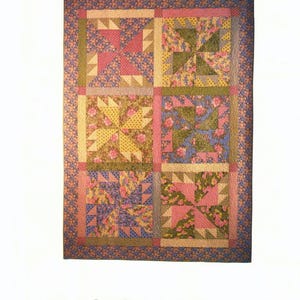 May include: A rectangular quilt featuring six square blocks with pinwheel patterns in shades of pink, yellow, green, and blue floral prints. The text below the quilt reads Rosebud Remembrance fun • fast • easy in dark blue lettering.