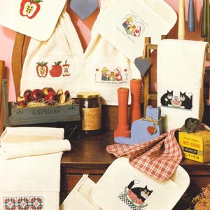 May include: A collection of embroidered kitchen towels and pot holders with various designs, including apples, cats, and hearts. The text "8 TOWEL AND POT HOLDER DESIGN" is at the top. Other text includes "Seasoned with love" and "Give us this day our daily bread".