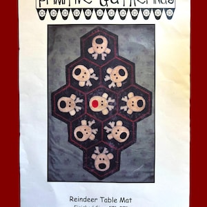 May include: A pattern for a reindeer table mat with a finished size of 17 inches by 27 inches. The pattern features a hexagon design with eight reindeer appliques and a red button in the center. The pattern is titled "Reindeer Table Mat" and has the product code "PRI-173".