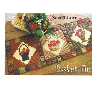 May include: A quilted table runner with a basket theme. The runner features three square panels with basket designs, surrounded by a border of small basket motifs. The text "Basket Time" is displayed at the bottom. The words "Need'l Love" are at the top.