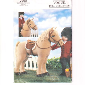 May include: A Vogue Doll Collection sewing pattern envelope, number 7603, featuring a tan plush horse with a brown saddle and bridle. A doll dressed in a red riding jacket and black helmet stands beside the horse. The background shows a white fence.