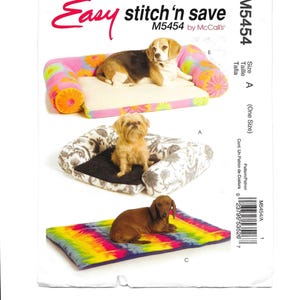 May include: A sewing pattern for dog beds, featuring three different designs. The top bed is a sofa style with a floral print, the middle bed has a floral pattern, and the bottom bed is a tie-dye mat. The text "Easy stitch'n save" is visible.