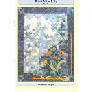 May include: A quilt titled "It's a New Day" with dimensions of 52" x 68". The quilt features a patchwork design in shades of blue, green, and white, with a dark blue border. Orange flowers with green stems are on the lower right.