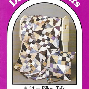 Puede incluir: Un juego de edredón y almohada con un diseño de patchwork geométrico en tonos beige, morado y marrón. El edredón está sobre una silla de madera. El texto "Dream Spinners" y "Pillow Talk" es visible.