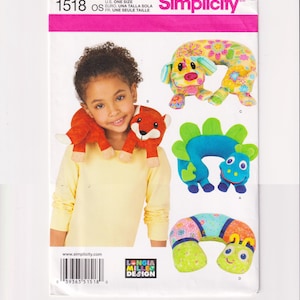 May include: A Simplicity sewing pattern envelope 1518 featuring illustrations of four different animal-shaped neck pillows: a fox, a floral dog, a blue dinosaur, and a colorful caterpillar. The package includes a barcode and the text Simplicity.